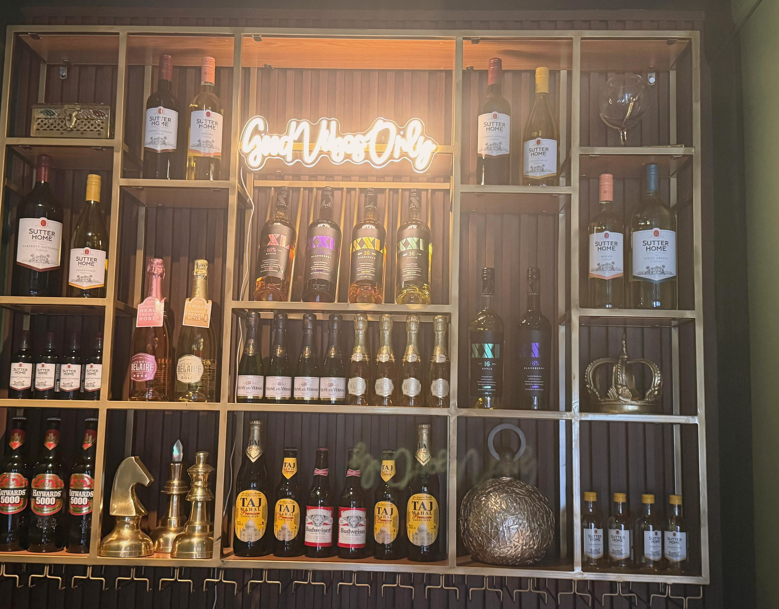 A brass-framed bottle wall with warm light and a neon sign